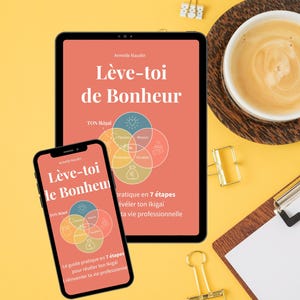 Może przedstawiać: Tablet i smartfon wyświetlają okładkę książki "Lève-toi de Bonheur" autorstwa Armelle Naudin, z diagramem TON Ikigai. Na żółtym tle filiżanka kawy, schowek na dokumenty i złote spinacze do papieru. Książka dotyczy samodoskonalenia.