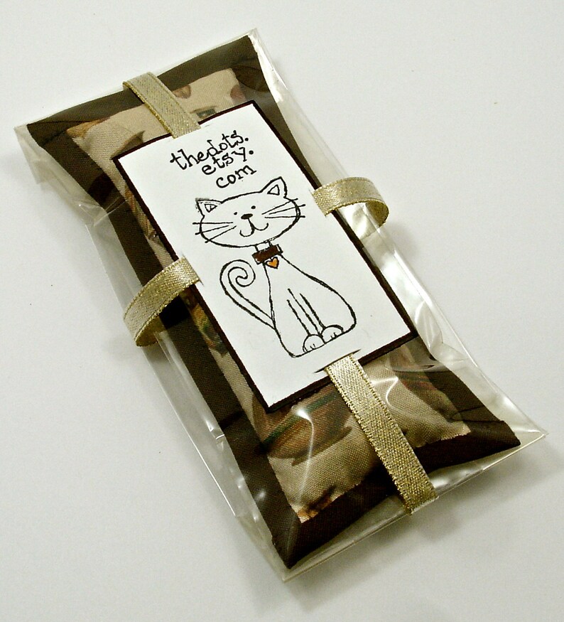 May include: A clear cellophane package containing a rectangular item with a brown border and a tan patterned center. A white tag with a cat illustration and the text "thedots.etsy.com" is attached with a gold ribbon.