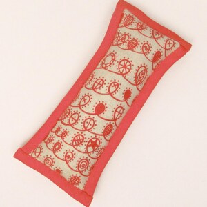 May include: A small, rectangular pillow with a light beige fabric and a red border. The fabric has a repeating pattern of red circles, stars, and other shapes.