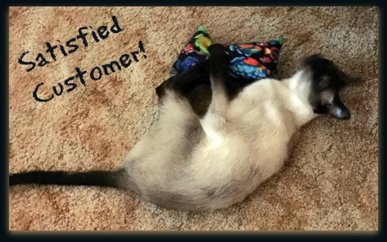 May include: A Siamese cat with cream-colored fur and dark points is lying on its back, paws up, next to a patterned pillow. The text "Satisfied Customer!" is written above the cat.
