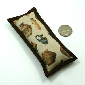 May include: A rectangular cat toy with a brown border. The beige fabric is printed with colorful illustrations of ancient pottery. A quarter is next to the toy for size comparison.