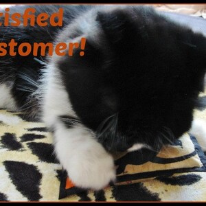 May include: A black and white cat is shown with the text "Satisfied Customer!" in orange. The cat is lying on a leopard print blanket and appears to be playing with a small toy.
