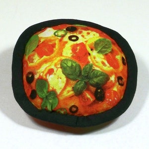 May include: A round, black-rimmed, fabric pizza toy with a colourful printed image of a pizza with toppings such as pepperoni, olives, and basil.