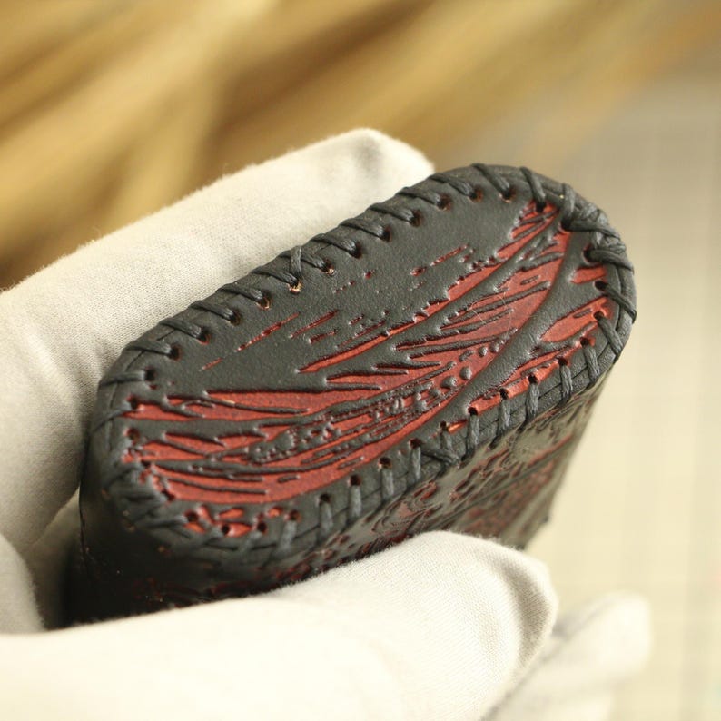 May include: A close-up of a black leather case with red detailing. The case has a stitched border and a textured surface. The red interior design features a pattern of lines and shapes.