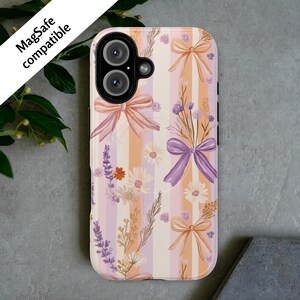 May include: A phone case with a floral design and a vertical striped pattern in peach, lavender, and cream. The case features illustrations of bows, daisies, and lavender sprigs. The text "MagSafe compatible" is visible.