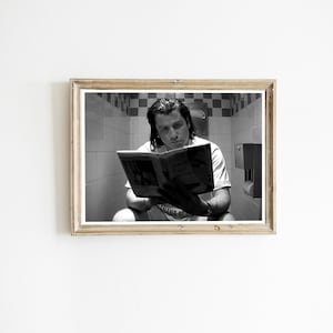 May include: Black and white framed print of a person reading a magazine while sitting on a toilet. The person is wearing a white t-shirt. The bathroom has white and black checkered tiles.