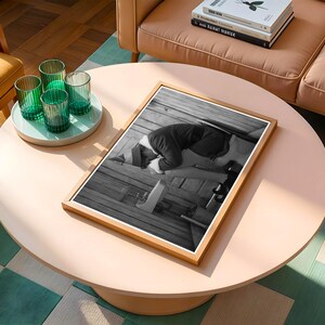 May include: A framed black and white photograph of a person kneeling on a wooden surface. The photograph is displayed on a light pink round coffee table. Four green ribbed glasses sit on a light blue tray.