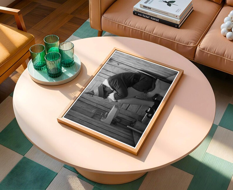 May include: A framed black and white photograph of a person kneeling on a wooden surface. The photograph is displayed on a light pink round coffee table. Four green ribbed glasses sit on a light blue tray.