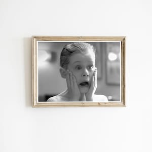 May include: Black and white framed print of a young person with a surprised expression, hands on cheeks, mouth open. The frame is a light brown color. The image is set against a white background.