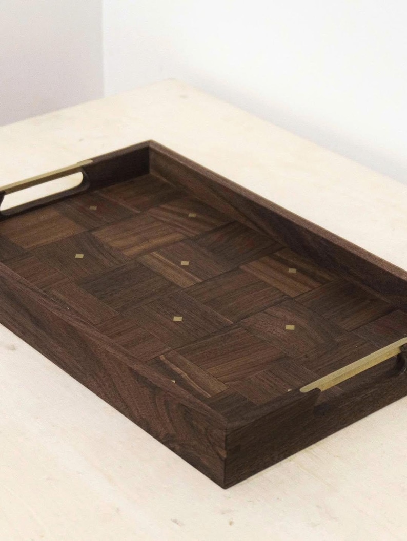 May include: A rectangular wooden serving tray with a dark brown, parquet-style surface. The tray has brass-colored handles and small brass accents. The tray is designed for serving food or drinks.