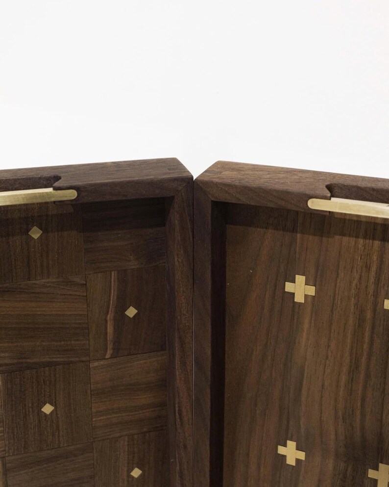 May include: Two wooden boxes with a dark brown finish. One box features a geometric pattern, while the other has gold cross inlays. Both boxes have gold-colored handles.