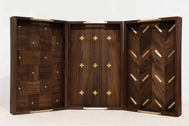 May include: A three-panel wooden tray set with a dark brown finish. The panels feature various inlaid patterns, including a patchwork design, crosses, and a chevron pattern. Gold-colored metal handles and accents are present.