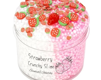 May include: A clear plastic container filled with strawberry-themed slime. The slime is divided into white and pink sections, with strawberry-shaped decorations on top. The text "Strawberry Crunchy Slime" is printed on the container.