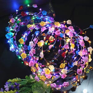 Puede incluir: Dos diademas florales con rosas multicolores y pequeñas luces LED. Las rosas son en tonos rosa, amarillo, azul y morado. Las luces son multicolores, creando un aspecto festivo y decorativo.