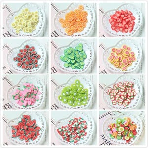 May include: A collection of fruit-shaped polymer clay slices, including bananas, oranges, strawberries, watermelon, limes, grapefruit, kiwi, and apples. Each fruit is arranged in a white, heart-shaped dish.