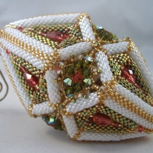 May include: A white, gold, and green beaded Christmas ornament with a geometric design. The ornament is shaped like a diamond and has a loop at the top for hanging.
