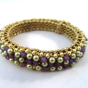 May include: Gold-toned beaded bracelet with rows of small, round beads and larger, pearlescent green beads. The bracelet also features purple crystal accents, creating a layered and textured design. A piece of jewelry.
