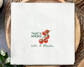 May include: White paper napkin with a diamond pattern. The napkin features the text "THAT'S AMORE" in green, along with a cluster of red tomatoes and the names "Lola & Martin" in green.