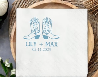 May include: White square paper napkin with a light blue illustration of two cowboy boots. The text "LILY + MAX" and the date "02.11.2025" are printed below the boots. The napkin is placed on a wooden tray.