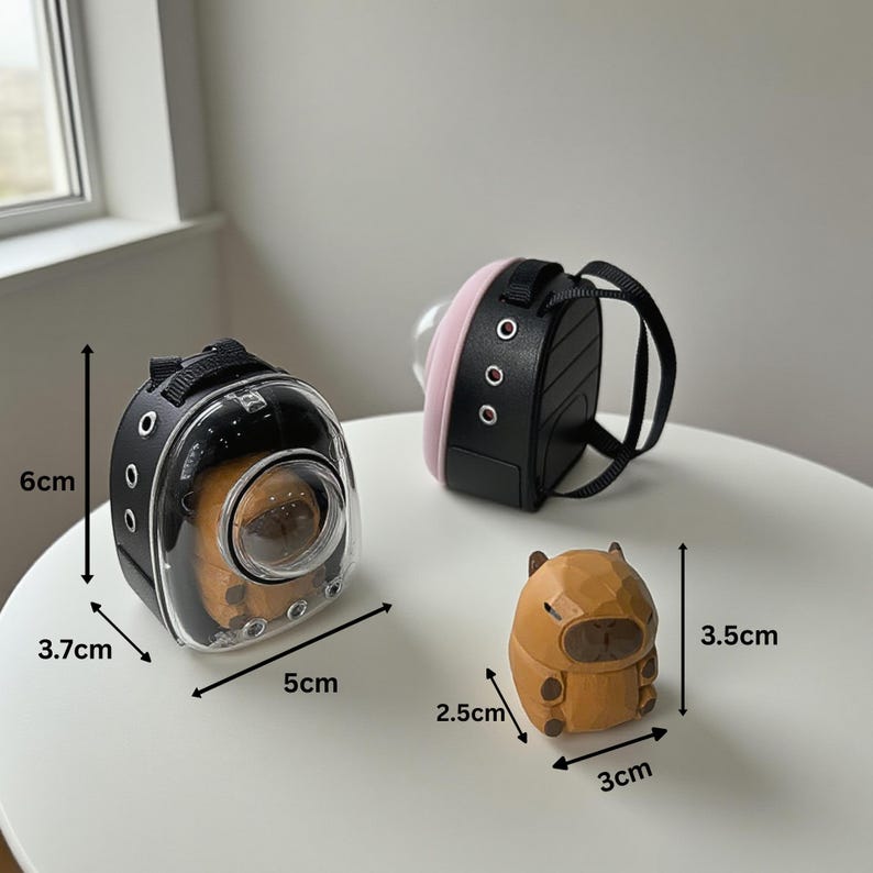May include: A clear and black pet carrier with a small animal inside, measuring 5cm long, 3.7cm wide, and 6cm tall. A black and pink backpack-style carrier and a small wooden figurine of an animal are also present.