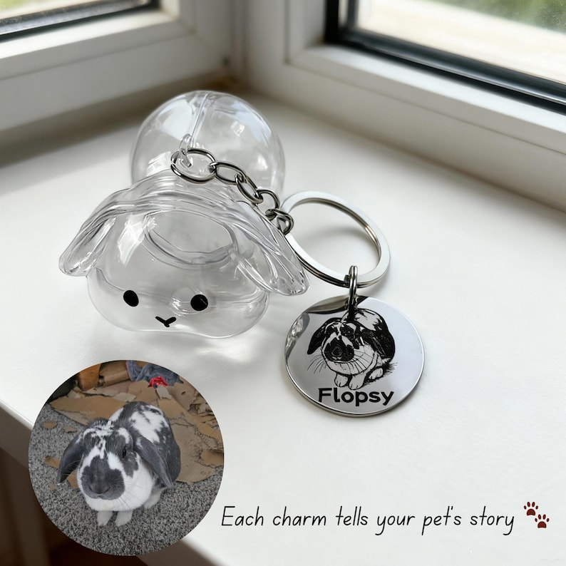 May include: A clear plastic bunny-shaped keychain with a silver keyring and a circular tag. The tag features a black and white illustration of a rabbit and the name "Flopsy". The text "Each charm tells your pet's story" is also visible.