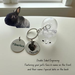 May include: A keychain with a clear bunny-shaped charm and two silver tags. One tag has the name "Tiberius" engraved, and the other features a black and white image of a bunny with the name "Tiberius". The text reads "Double Sided Engraving".