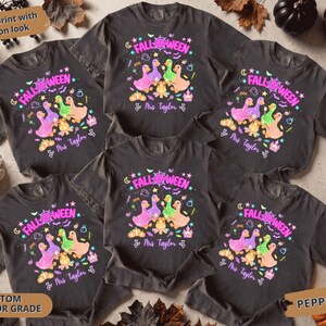Puede incluir: Cinco camisetas de manga corta en color gris carbón con un estampado gráfico que incluye el texto FALL-WEEN y Mrs Taylor. El diseño muestra tres patos coloridos, una fogata, calabazas, estrellas y murciélagos en tonos neón.