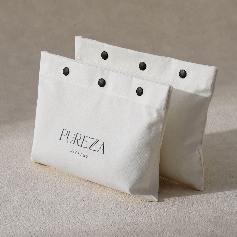 May include: Two off-white canvas pouches with black snap closures. The word "PUREZA" is printed in black, with "PACKAGE" below it. The pouches are rectangular and appear to be made of a sturdy fabric.