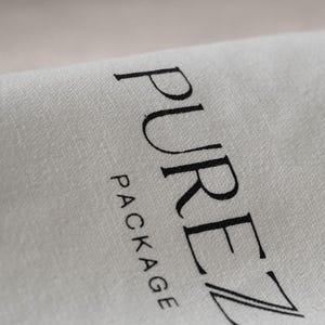 May include: Close-up of a light gray fabric with the words "PUREZ PACKAGE" printed in black. The fabric appears to be folded, with the text slightly curved along the fold.
