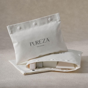 May include: Two white canvas pouches with snap closures, one open to reveal small, light-coloured cosmetic products. The top pouch displays the text "PUREZA PACKAGE" in black. The pouches are arranged on a neutral-toned surface.
