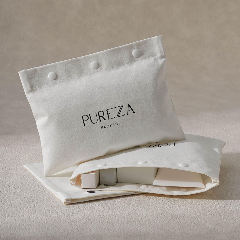 May include: Two white canvas pouches with snap closures, one open to reveal small, light-colored cosmetic products. The top pouch displays the text "PUREZA PACKAGE" in black. The pouches are arranged on a neutral-toned surface.