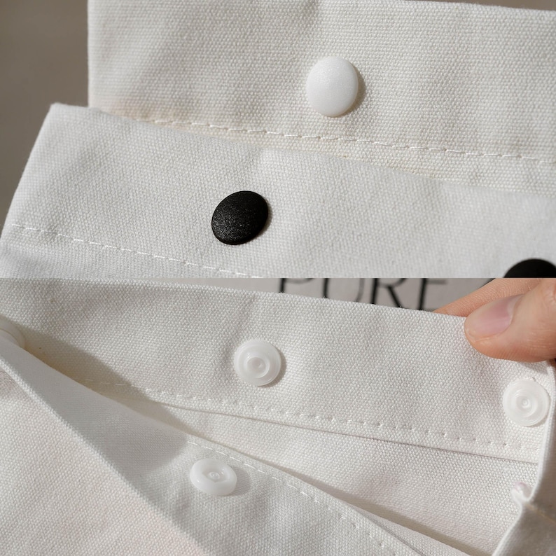 May include: Close-up of white fabric with black and white buttons. The fabric appears to be a shirt collar or similar garment detail. The buttons are round and sewn onto the fabric. The image is well-lit, highlighting the texture of the fabric.