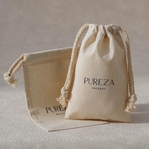 Puede incluir: Dos bolsas beige con cordón. Una bolsa está de pie, mostrando el texto "PUREZA PACKAGE" en negro. La otra bolsa está plana. Ambas bolsas tienen un aspecto natural y texturizado y están hechas de una tela de color claro.