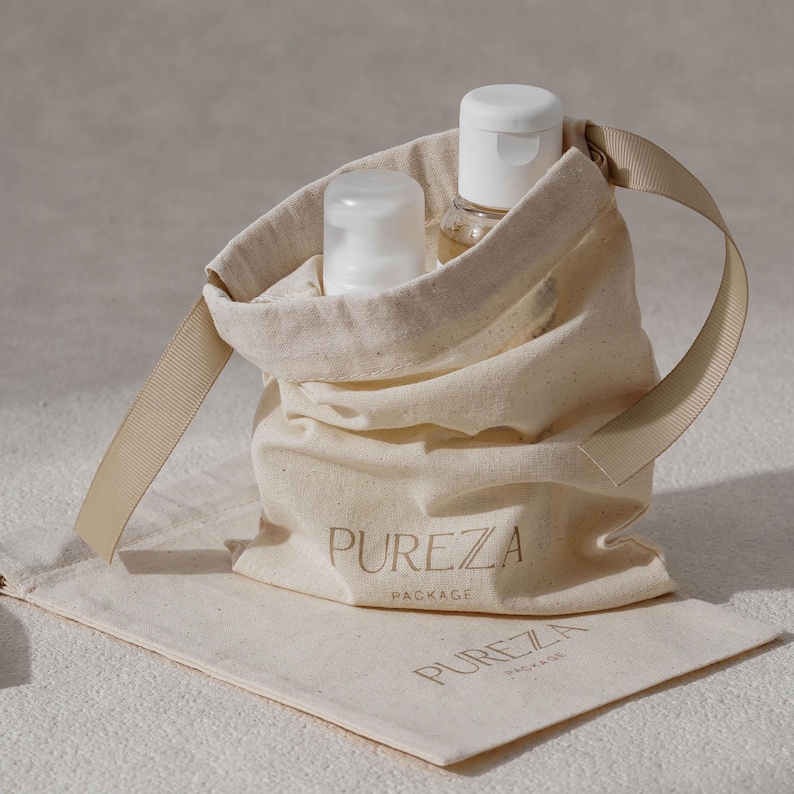 K&ouml;nnte beinhalten: Ein beigefarbener Stoffbeutel mit Kordelzug und einem Bandgriff, auf dem der Text PUREZA PACKAGE aufgedruckt ist. Im Beutel befinden sich zwei wei&szlig;e Kunststoffflaschen mit Pumpspendern. Ein passender flacher Stoffbeutel liegt darunter.