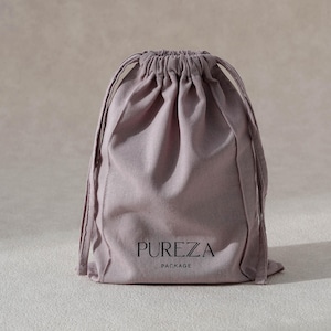 May include: A mauve drawstring bag with the text "PUREZA PACKAGE" printed in black. The bag is made of a soft fabric and has a gathered top with drawstrings.