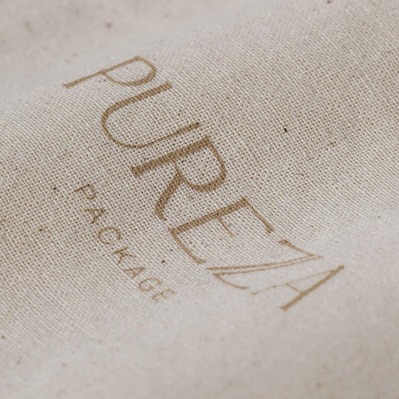 K&ouml;nnte beinhalten: Eine beige, texturierte Stoffoberfl&auml;che mit dem Wort PUREZA, das in einer gro&szlig;en, braunen serifenlosen Schrift gedruckt ist, wobei das Wort PACKAGE in einer kleineren, braunen Schrift direkt unter dem Buchstaben P steht.