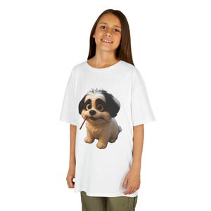 Könnte beinhalten: Weißes T-Shirt mit einem Cartoon-Hund-Design. Der Hund hat schwarz-weißes Fell und hält einen braunen Stock. Das T-Shirt hat eine lockere Passform, wobei die Hunde-Grafik im Mittelpunkt steht. Der Hintergrund ist schlicht weiß.