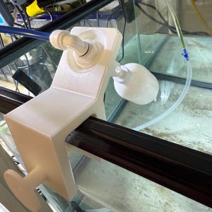 May include: A white aquarium filter holder with a clamp and a round knob. The holder is attached to the edge of a glass aquarium. A clear tube is connected to the filter holder.