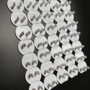May include: A collection of white plastic outlet plug covers. Each cover has a circular base with two prongs extending upwards. The covers are arranged in a grid pattern against a dark background.