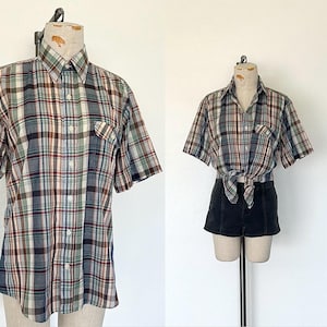 May include: A short-sleeved plaid shirt in shades of green, brown, and blue, displayed on a mannequin. The shirt has a button-down front, a chest pocket, and a classic collar. The second image shows the shirt tied at the waist with black shorts.