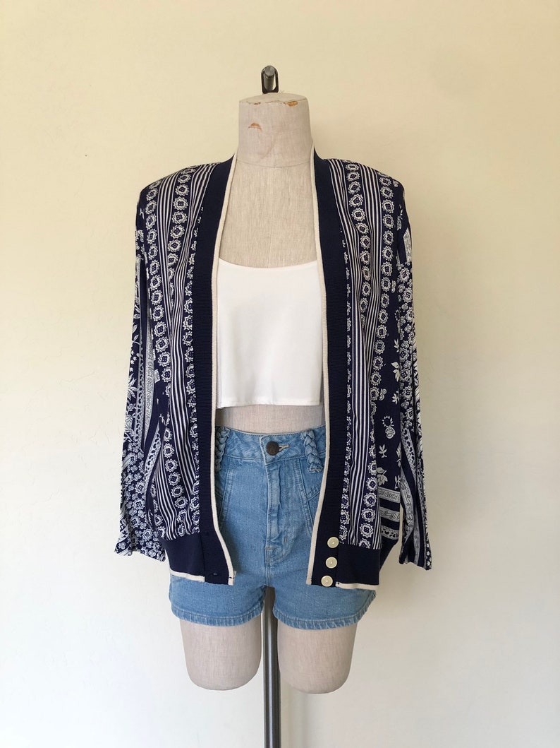 May include: A navy blue cardigan with a white and blue patterned design. The cardigan has a button closure and long sleeves.