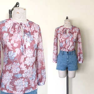 May include: A pink and blue floral print blouse with a tie at the neckline. The blouse has long sleeves and a relaxed fit.