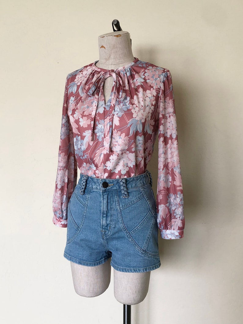 May include: A floral print blouse with a tie at the neck and long sleeves. The blouse is paired with denim shorts.