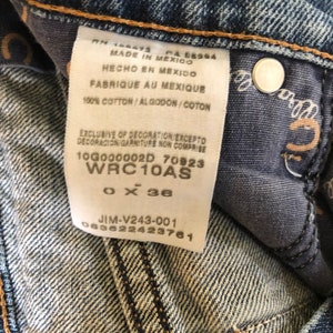 May include: Close-up of a pair of blue denim jeans. The jeans have a white tag with text in English, Spanish, and French. The tag includes the text "MADE IN MEXICO" and "100% COTTON". The jeans are size 36 inches.