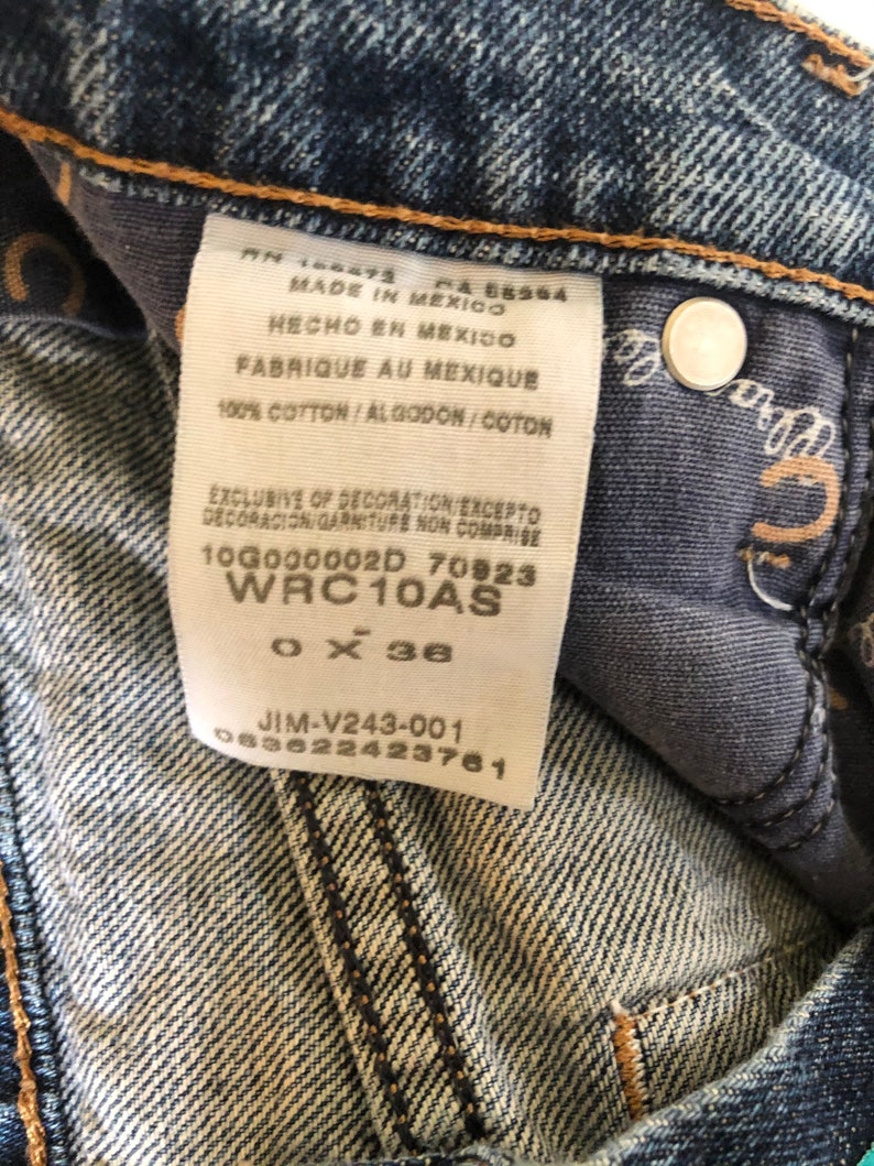 May include: Close-up of a pair of blue denim jeans. The jeans have a white tag with text in English, Spanish, and French. The tag includes the text "MADE IN MEXICO" and "100% COTTON". The jeans are size 36 inches.