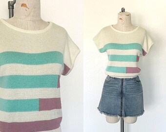 Op de afbeelding: Een witte, turquoise en mauve gestreepte gebreide trui met korte mouwen. De trui is op een witte mannequin.