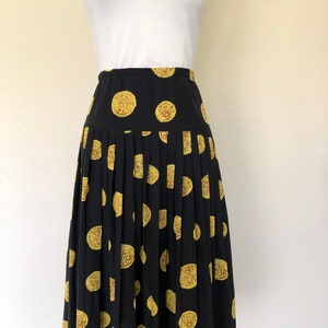 Op de afbeelding: Een zwarte geplooide rok met een gouden en bruine koekprint. De rok is midi-lang en heeft een aansluitende taille.