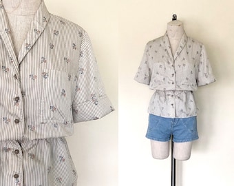 May include: A striped and floral patterned button-up shirt with short sleeves and a cinched waist. The shirt is on a white mannequin.