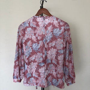 May include: A long-sleeved blouse with a pink and blue floral print. The blouse has a round neckline and a zipper closure in the back.