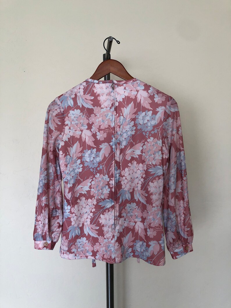 May include: A long-sleeved blouse with a pink and blue floral print. The blouse has a round neckline and a zipper closure in the back.